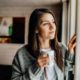 Girl holding coffee cup looking out window